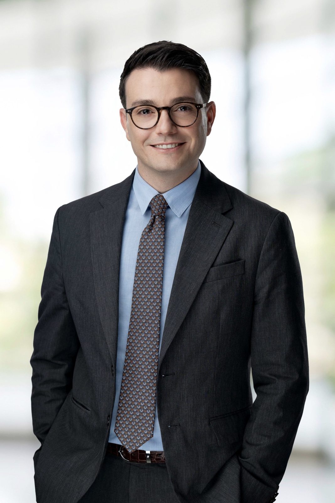 Portrait of Evren Kurt, smiling, in a charcoal suit, blue shirt and patterned tie